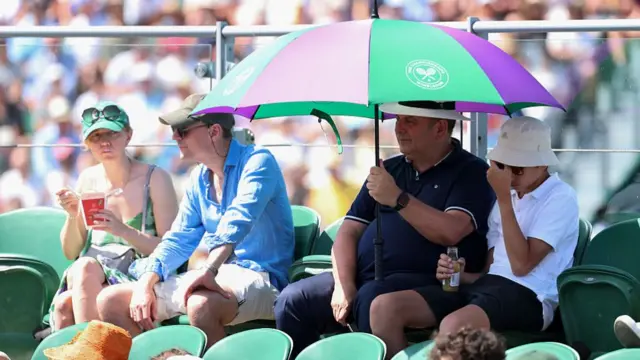 Spectators watch at Wimbledon under an umbrella