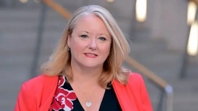 Christina McKelvie smiles in Holyrood's Garden Lobby wearing a red blazer and a necklace