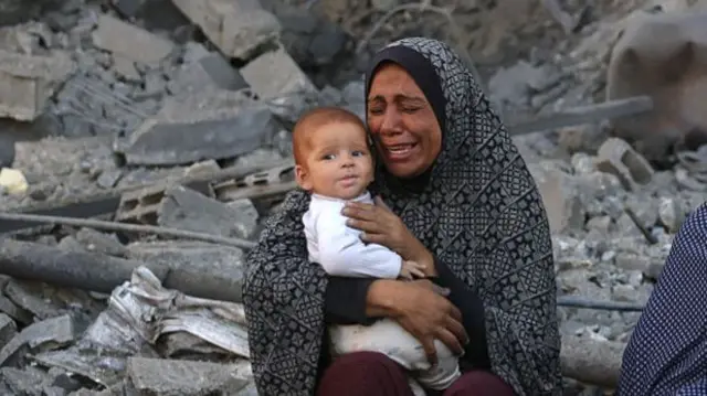 A woman crying as she sits among rubble holding a baby