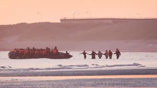 A group of people approaching a small boat at France, in an attempt to reach the UK by crossing the English Channel.