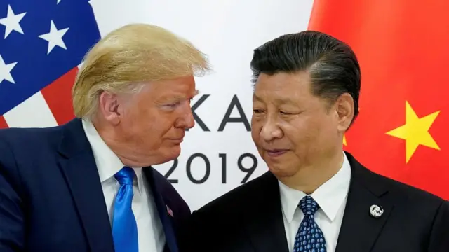 A file photo of Trump and Xi meeting. The two men stand shoulder to shoulder, heads turned towards one another. Their two countries' flags are behind them