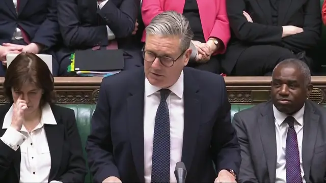 Starmer stands in the House of Commons, others sit either side of him
