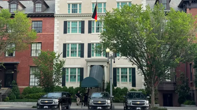 Two men stand outside Blair House in Washington DC, from a second-storey window a German flag hangs