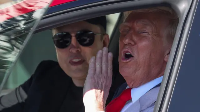 Trump calls out to media from inside a Tesla vehicle, with Musk sat behind him.