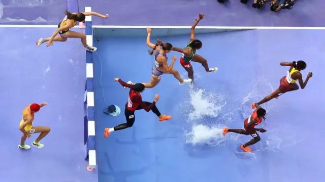Female athletes jump into water in the Women's 3000m Steeplechase at the Paris Olympics.