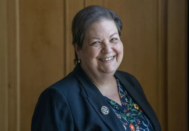 Labour MSP Jackie Baillie smiles wearing a blue jacket and flowery blouse