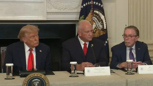 Donald Trump sits with two men at a meeting table