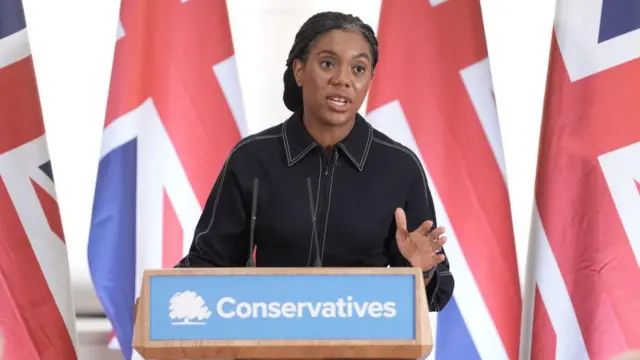 Kemi Badenoch makes a speech in front of a Conservatives podium.