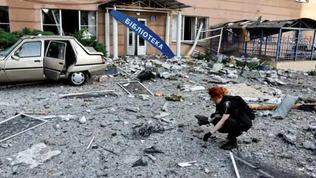 A uniformed officer inspects debris among the rubble outside a bombed building in Kyiv