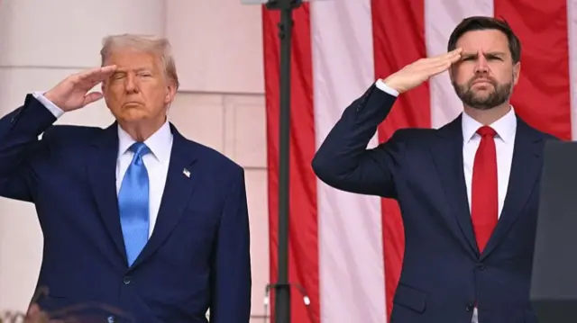 Donald Trump and JD Vance stood beside each other, both saluting, US flag behind them.
