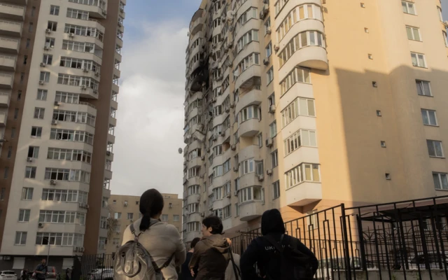 People look up at two buildings that were hit and partially destroyed in the city of Kyiv, Ukraine