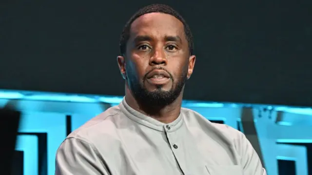 Diddy wearing a grey shirt, sitting down, looking into the camera