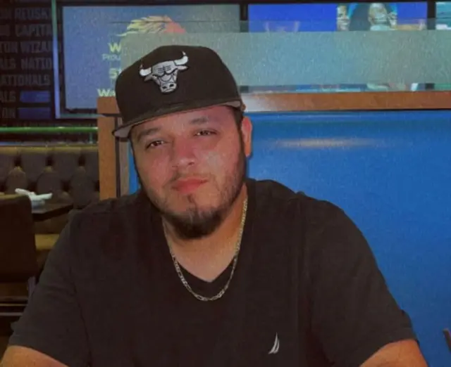 Kilmar Ábrego García wearing a black top, black hat with a bull on and silver chain