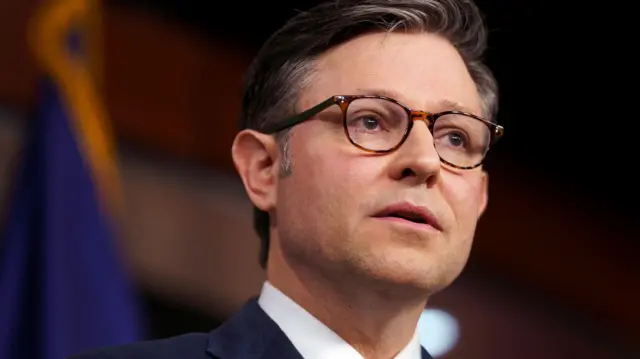 Mike Johnson wearing red tie, black suit, white shirt and brown glasses