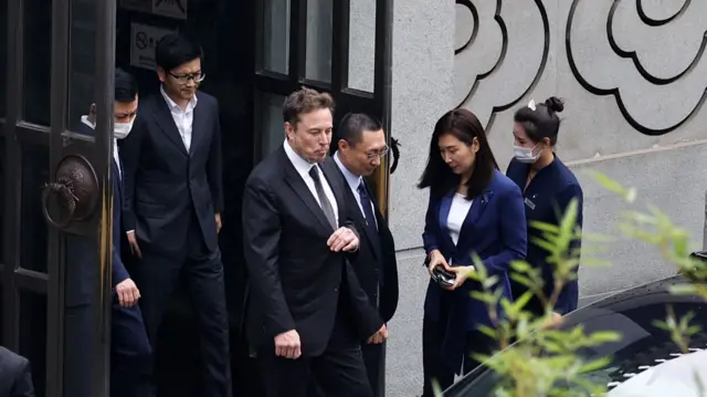 Musk, flanked by several other people in suits, leaves a restaurant in Beijing, China.