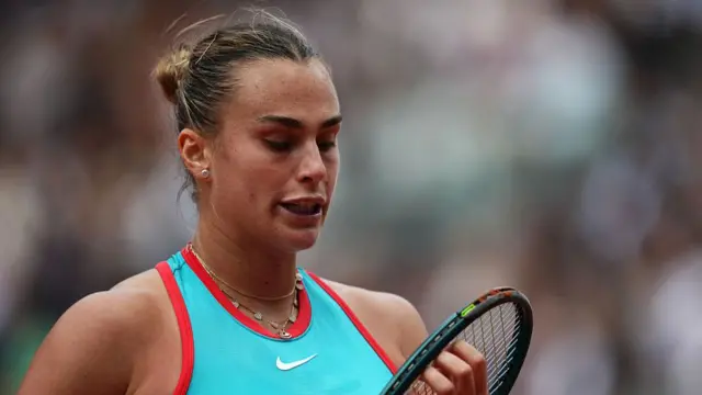 Aryna Sabalenka checks her racquet