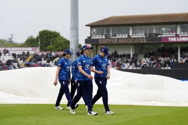 England's Kate Cross walks off with team-mates as ground staff deploy covers as rain halts play during the third Women's One Day International match at The Cooper Associates County Ground, Taunton