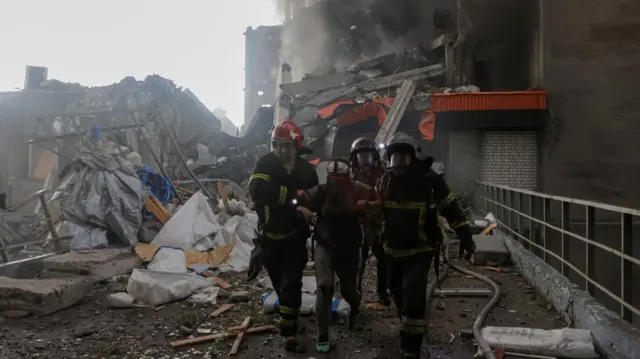 Rescuers assist an injured resident after she was released from debris of a building hit by a Russian drone strike