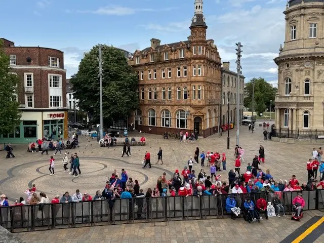 A view of Queen Victoria Square in Hull as fans, wearing predominantly red and white, gather near a metal security barrier.