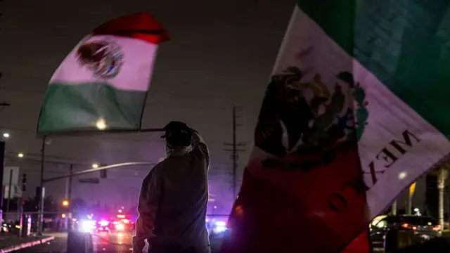 Demonstrators wave large Mexico flags as police cars are seen lined up in the distance