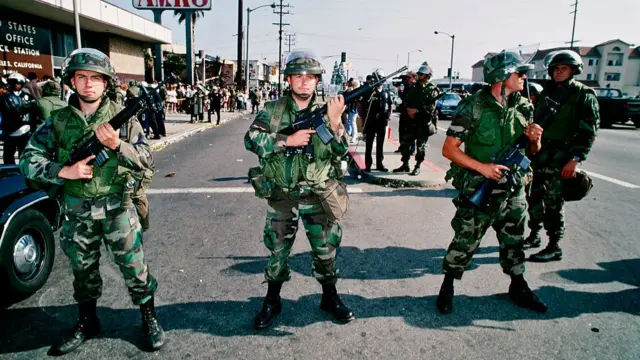 Members of the national guard stand in the middle of the street in military fatigues holding guns in downtown LA