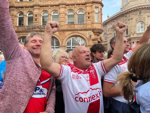 Two fans hold their arms in the air