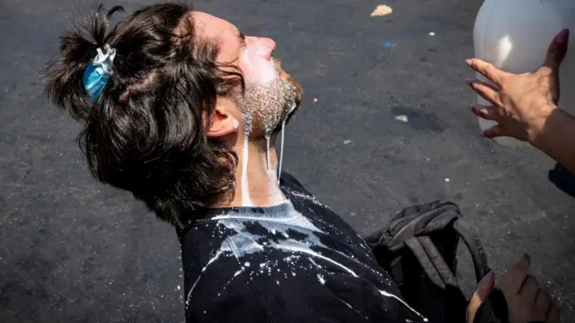 A man is seen kneeling on the ground as milk - often used as a treatment for tear gas - is poured onto his face