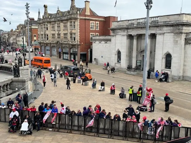 Fans gather near a metal security barrier in Queen Victoria Square, Hull. The Ferens Art Gallery, a grey coloured, building is visible in the background.