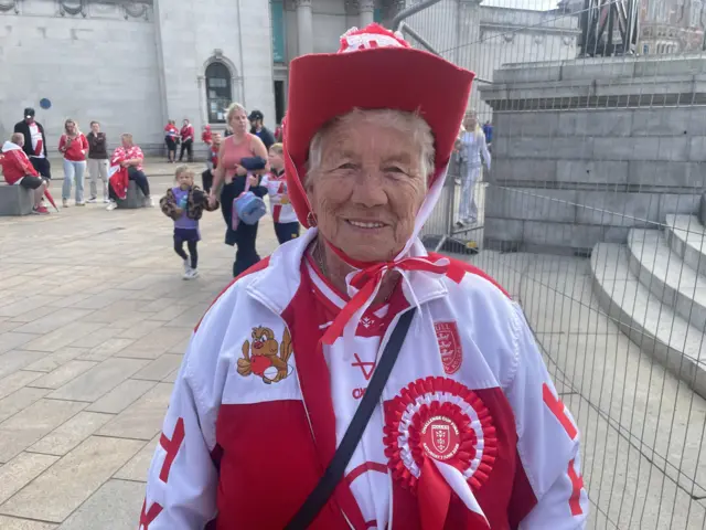 A woman wearing a red cowboy hat, red and white jacket and a red and white rosette smiles into the camera.