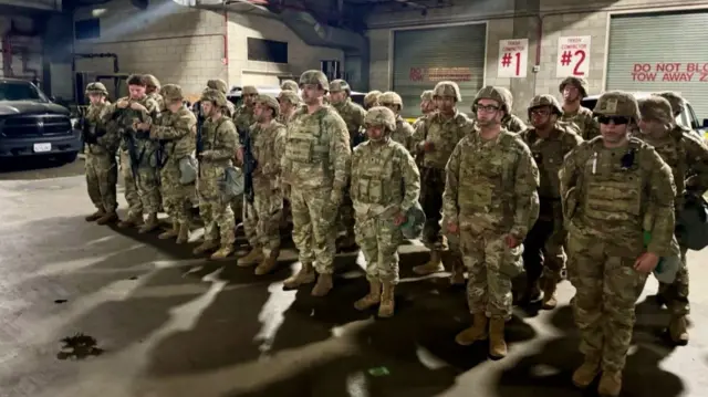 Troops stand in what appears to be a parking area