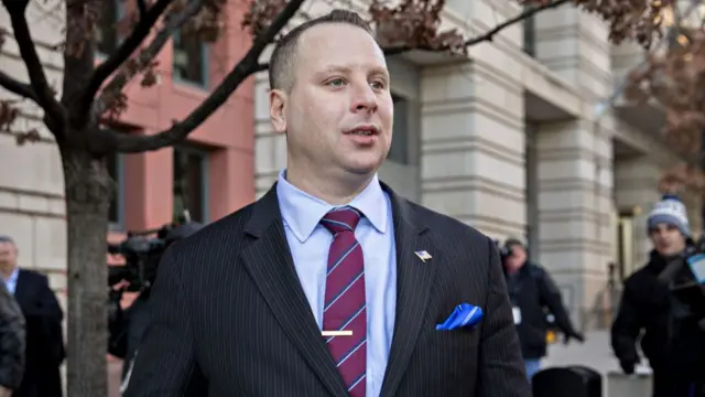 Sam Nunberg leaving a building wearing a black striped suit with light blue shirt, striped burgundy tie