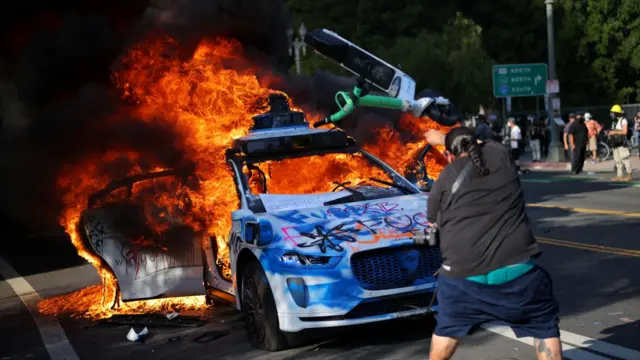 A protester throws an electric scooter on a burning vehicle during demonstrations in Los Angeles.