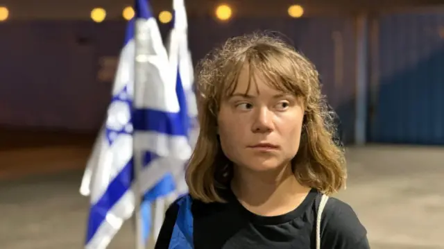 A picture of Greta Thunberg. She is looking to the side and two Israeli flags can be seen behind her