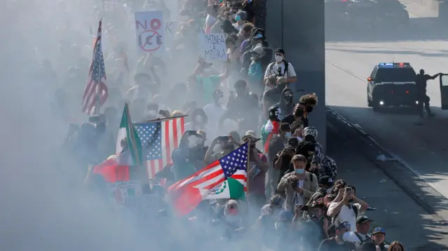 Demonstrators are seen behind white smoke, holding American and Mexican flags.
