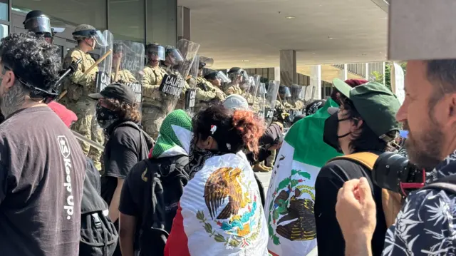 A crowd of protesters face a line of National Guardmen on the steps of a federal building