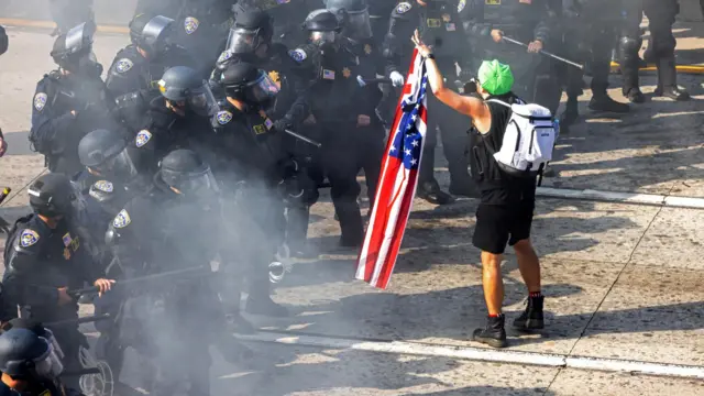 A lone demonstrator holds an American flag as he stands in front of a row of armed police officers in Los Angeles.