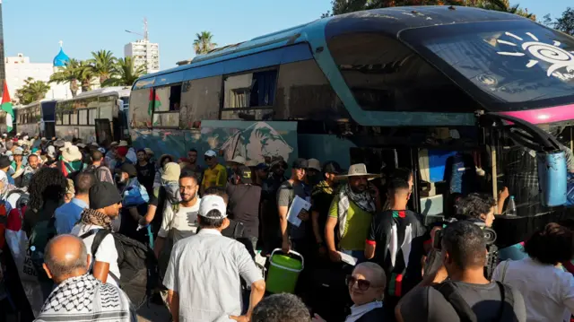 Participants of a Tunisian-led land convoy crowd around a bus and board the bus