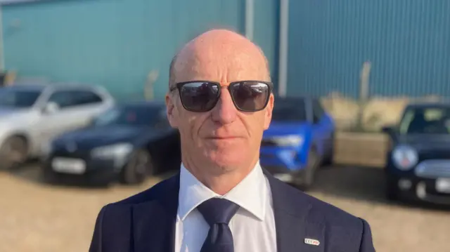 Kevin Keable wearing a dark suit and tie with a white shirt, he is wearing sunglasses