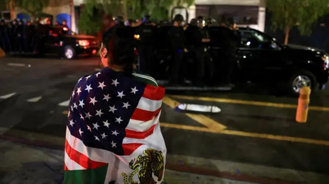 A demonstrator wrapped in a flag looks on as police officers patrol during LA immigration protests in downtown Los Angeles on 8 June 2025