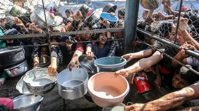 People in Gaza putting bowls underneath a metal fence trying to get food.