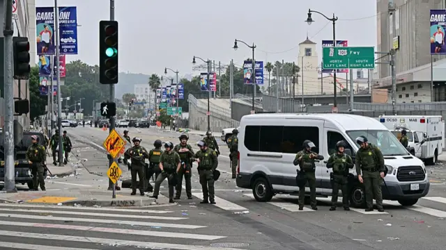 Officers with the LA County Sheriff's Office stand in the litter-covered streets of downtown LA following anti-ICE raids protests. The group are in full protection gear with helmets and bullet-proof vests next to a white van