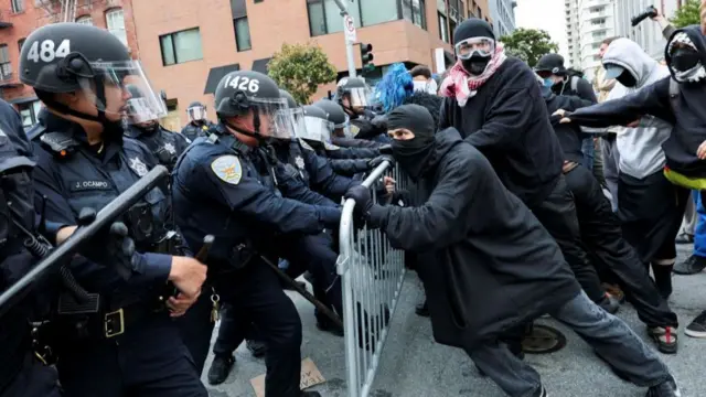 Police and protesters push on either side of a metal railing