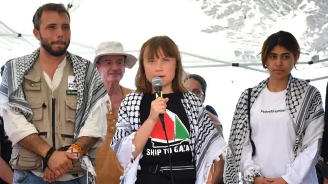 Greta Thunberg speaking into a microphone with other activists behind her
