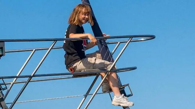 Greta Thunberg sitting on the tip of the ship, wearing a black T-shirt