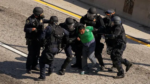 Several police officers detain a man, wearing a green t-shirt, during demonstrations in Los Angeles.