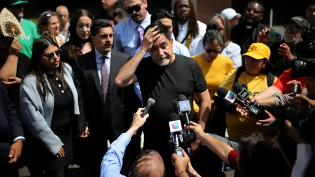 Huerta holds a hand to his forehead as he speaks into microphones held towards him by journalists