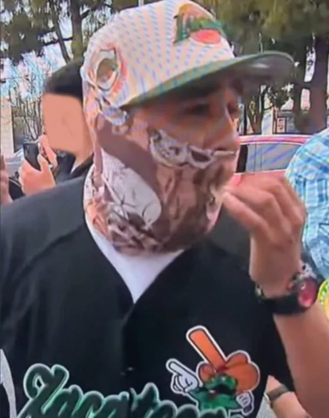 A man wearing a colourful cap, cover over his mouth and lower neck in Black baseball shirt