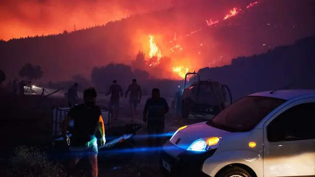 People and firefighters attempt to extinguish the flames as smoke and flares rise from a forested area following a wildfire in the Seferihisar district of Izmir