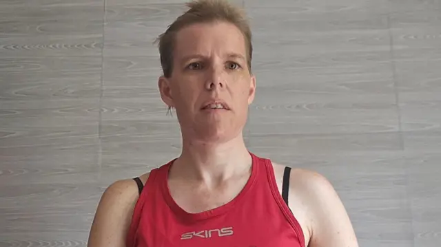Stacy sits in a room with a grey background wearing a red top