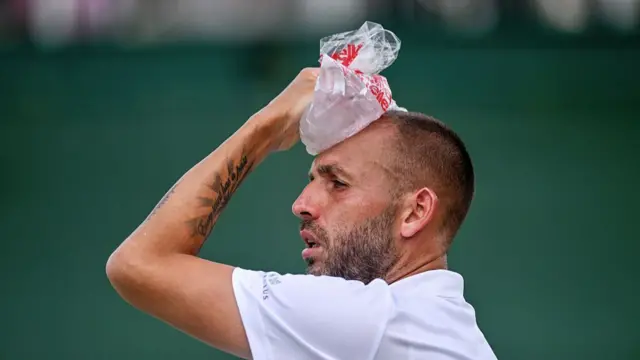Tennis player holds a packet of ice over his head during a break in play